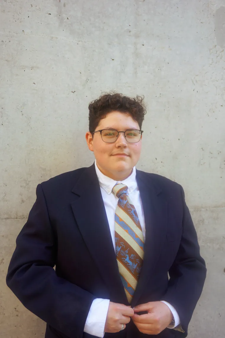 A photo of Francisco wearing a dapper navy suit with a white undershirt and a striped brown, cream, and light blue tie.